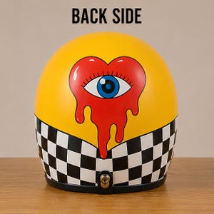 May include: A yellow motorcycle helmet featuring a black and white checkered pattern along the bottom edge. The centre displays a large red heart with a blue eye in the middle, appearing to drip downward. The text BACK SIDE is printed above.