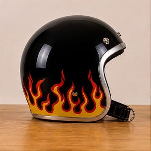 Può includere: Un casco aperto nero lucido con un vivace motivo a fiamme gialle e rosse lungo il bordo inferiore. Il casco presenta una finitura argentata attorno all'apertura, bottoni a pressione metallici e un cinturino nero con chiusura a anello a D.