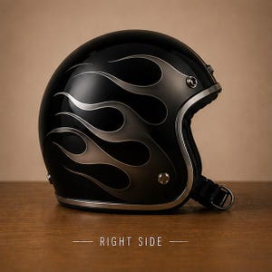 Könnte beinhalten: Ein glänzend schwarzer Jethelm für Motorräder mit einem silbernen Flammendesign an der Seite. Der Helm verfügt über eine metallisch silberne Kante, sichtbare Metallbeschläge und einen schwarzen Kinnriemen mit einem D-Ring-Verschlussmechanismus.
