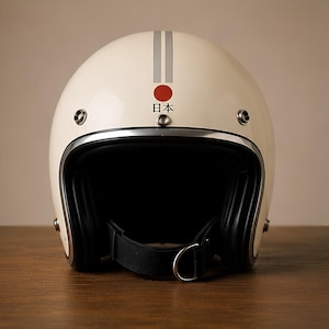 Puede incluir: Un casco de moto abierto de color blanco roto con una franja gris vertical, un emblema circular rojo y los caracteres japoneses para Japón. El casco tiene un forro interior negro, un borde cromado y una correa de barbilla negra con anilla en D.