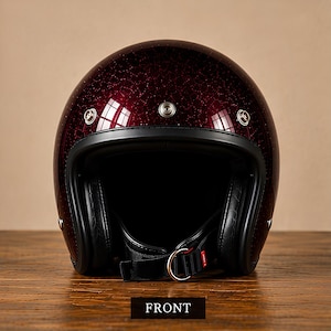 May include: A deep burgundy open-face motorcycle helmet with a glittery finish. The helmet features a black trim, three silver-toned metal snaps across the forehead, and a black chin strap with a metal D-ring closure. The word FRONT is printed below.