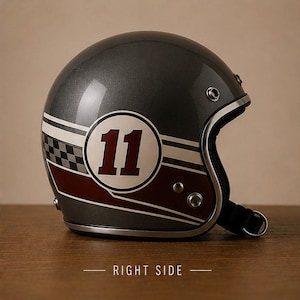 Puede incluir: Un casco de moto abierto de color gris carbón metalizado que presenta un emblema circular blanco con el número 11 en rojo oscuro, acentuado por rayas blancas horizontales y un patrón de cuadros negro y gris en el lateral, con borde plateado.