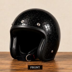 May include: A black open-face motorcycle helmet with a glittery finish, featuring a black trim, three silver-toned metal snaps along the forehead, and a chin strap with a D-ring closure. The word FRONT is printed in white on a black rectangle.