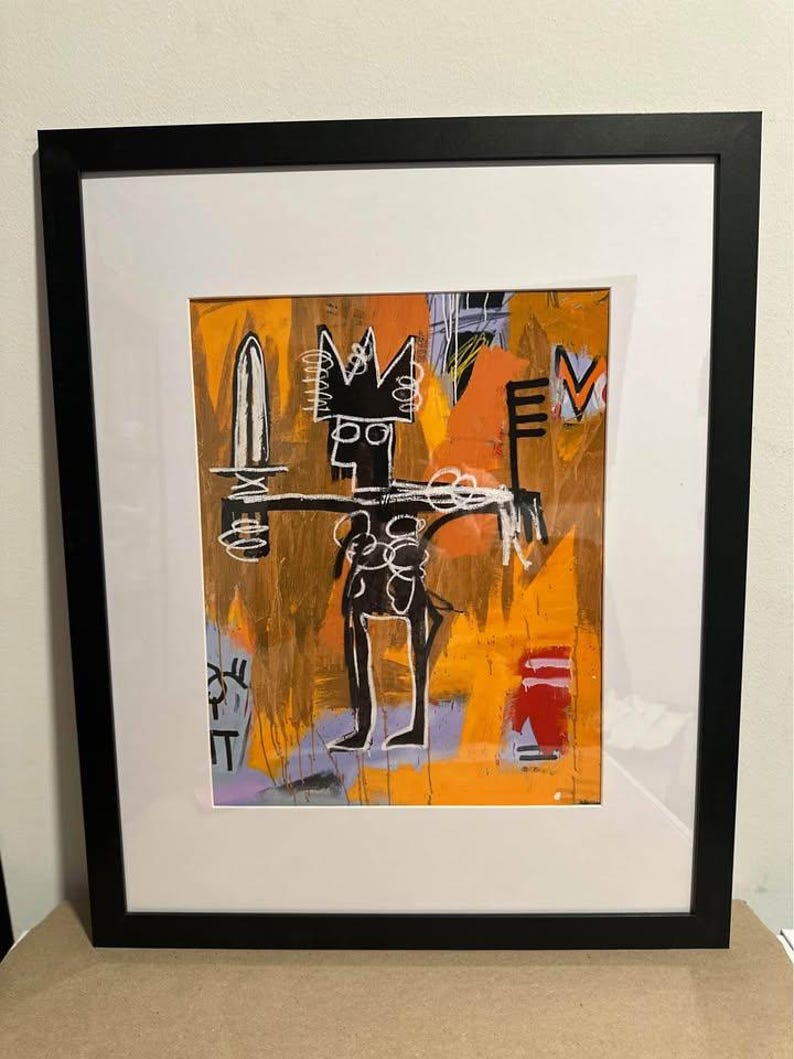 May include: Abstract art print in a black frame. The artwork features a black figure with a crown, holding a sword and a key, set against an orange and yellow background. The style is reminiscent of Basquiat.