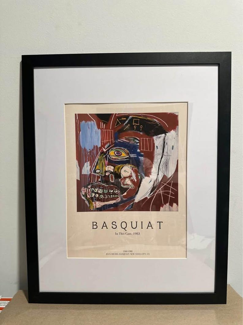 May include: Framed art print of a Basquiat abstract portrait. The artwork uses bold brushstrokes and a mix of colours, including red, blue, and yellow. The print is set in a black frame with a white mount.