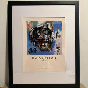 May include: Framed art print of a Basquiat skull painting. The artwork uses blue, yellow, and black brushstrokes. The print is in a black frame with a white mount, and the text "BASQUIAT" is visible.