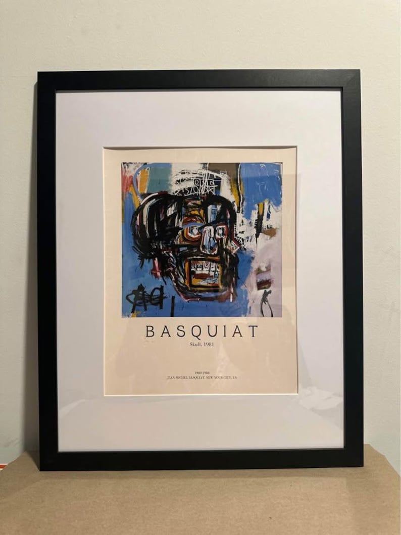 May include: Framed art print of a Basquiat skull painting. The artwork uses blue, yellow, and black brushstrokes. The print is in a black frame with a white mount, and the text "BASQUIAT" is visible.
