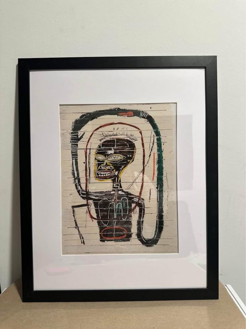 May include: Framed artwork depicting a stylized figure with a black head and torso, yellow face, and red and green accents. The artwork is set against a light-coloured, textured background and framed in a black frame with a white mount.