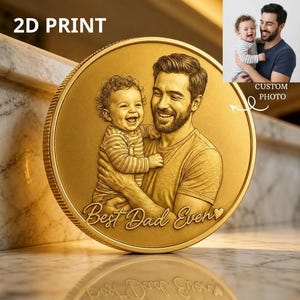 May include: A gold-colored coin with a 2D print of a father holding a baby. The coin has the words "Best Dad Ever" engraved on it. A smaller image shows the original photo used for the coin.