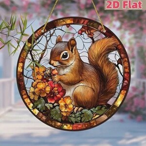 May include: A round, stained-glass window decoration featuring a brown squirrel holding a nut, surrounded by colorful flowers. The artwork is framed with a mosaic-style border and includes the text "2D Flat". A gold string is attached for hanging.