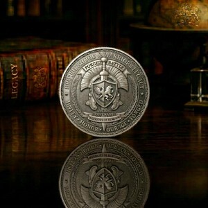 May include: A silver coin with the words "Brotherhood & Warriors Legacy" and "Forged Battle" engraved around the edge. The coin features a shield with a bird and a lion, and the words "Unity, Honor, Courage, Forged".