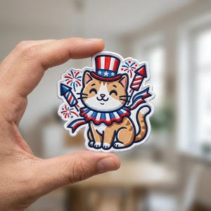 May include: An embroidered patch featuring a tan tabby cat wearing a red, white, and blue striped top hat with stars. The cat has a ruffled collar and is surrounded by red and blue fireworks and rocket motifs in a patriotic color scheme.