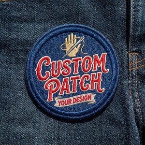 May include: A circular embroidered patch with a dark blue background and a thick blue border. The patch features a gold hand icon with a needle and thread, the red text CUSTOM PATCH, and a white banner with the red text YOUR DESIGN.