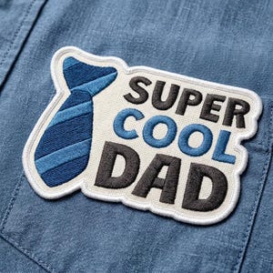 May include: Embroidered patch with the words "SUPER COOL DAD" in black and blue lettering, and a blue tie graphic. The patch is on a blue denim shirt pocket.