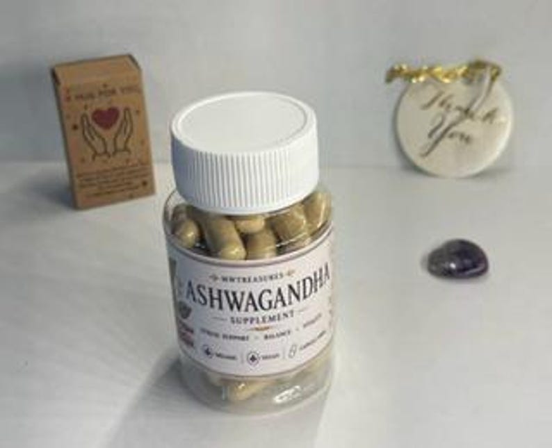 May include: A clear plastic bottle filled with tan capsules labeled "Ashwagandha Supplement." A small cardboard box with the text "A hug for you" and a "Thank You" gift tag are in the background. A small purple stone is also visible.