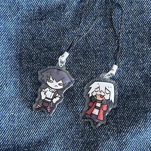 Könnte beinhalten: Zwei Acryl-Anhänger mit stilisierten Anime-Figuren und schwarzen Kordelschlaufen. Eine Figur hat dunkles Haar und ein weißes Hemd, die andere hat weißes Haar und eine rote Jacke. Beide Anhänger sind transparent und mit Metallringen versehen.