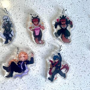 May include: Five acrylic charms featuring anime-style characters. The characters are in various poses and outfits, with vibrant colors and detailed designs. Each charm has a silver-colored keychain attachment.