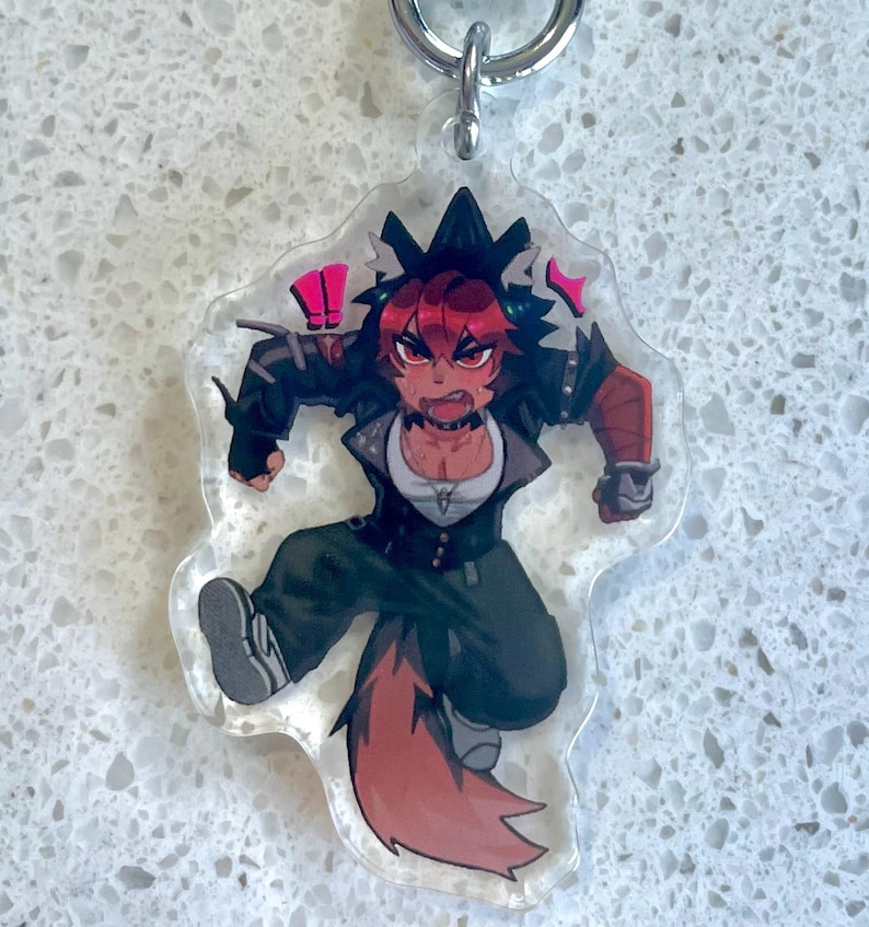 May include: A clear acrylic keychain featuring a dynamic anime-style character with red hair and a fox tail. The character is wearing a black jacket, white shirt, and dark green pants. The keychain has a silver metal ring.