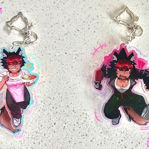 May include: Two anime-style keychains featuring a character with red hair and wolf ears. One keychain shows the character holding a bowl of food, wearing a pink apron. The other keychain shows the character in a fighting pose.