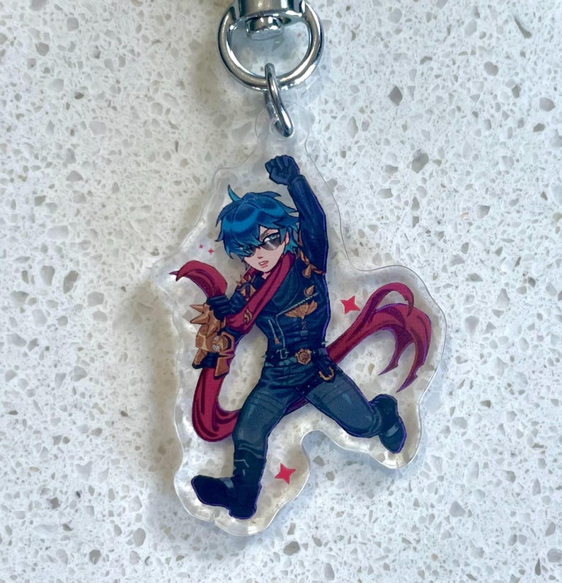 May include: A clear acrylic keychain featuring a cartoon character with blue hair, sunglasses, and a red scarf. The character is wearing a black outfit and is in a dynamic pose. The keychain has a silver metal clasp.