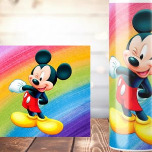 K&ouml;nnte beinhalten: Ein farbenfrohes Bild von Mickey Mouse in seiner klassischen Kleidung: schwarze Shorts, rote Shorts, gelbe Schuhe und wei&szlig;e Handschuhe. Der Hintergrund ist ein Regenbogenverlauf. Das Bild befindet sich auf einer rechteckigen Leinwand und einem zylindrischen Becher.
