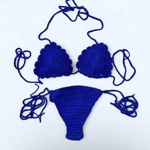 Op de afbeelding: Een handgemaakte, blauwe gehaakte bikiniset. De top heeft geschulpte randen en verstelbare bandjes. De onderkant is een klassieke bikinislip met bijpassende bandjes. De set wordt op een witte achtergrond gepresenteerd.