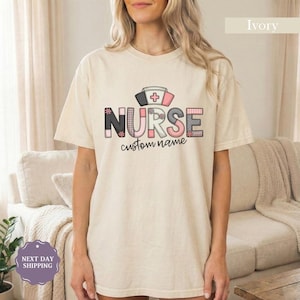 Peut inclure: T-shirt couleur ivoire avec le mot "NURSE" dans une police décorative, avec une coiffe d'infirmière et un symbole de croix. Le texte "custom name" est en dessous du mot "NURSE". Le t-shirt est de style décontracté à manches courtes.