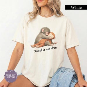 May include: White t-shirt featuring a graphic of two hugging monkeys. One monkey is gray, the other is brown. The text "Punch is not alone" is printed below the image in black.