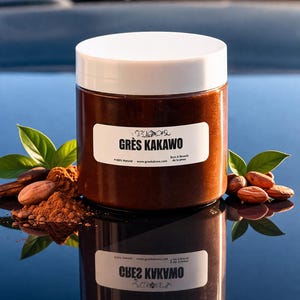 May include: A brown jar with a white lid, labeled "GRÈS KAKAWO", sits on a reflective surface. Cocoa beans, powder, and green leaves surround the jar. The text "100% Natural" and website address are also visible.