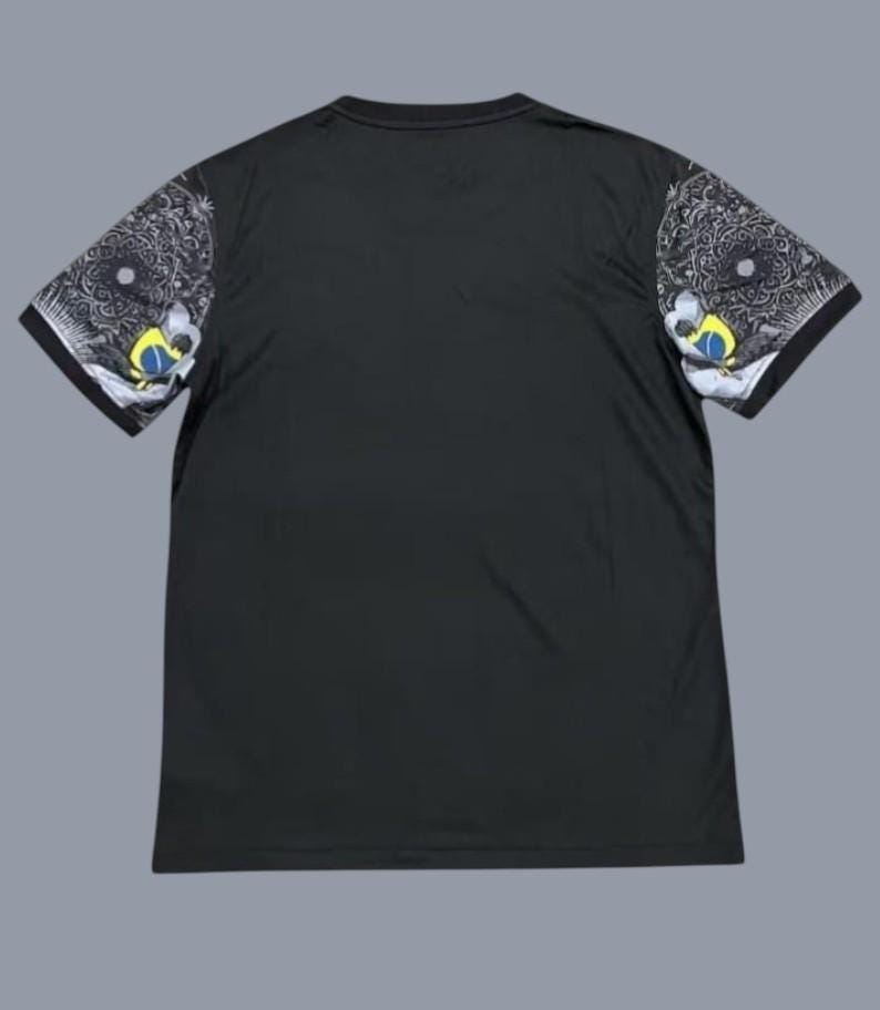 May include: Black t-shirt with short sleeves. The sleeves feature a detailed design in black, white, yellow, and blue. The design includes a circular pattern and a stylized eye. The shirt has a crew neck.
