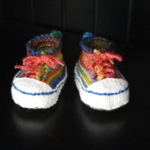 Puede incluir: Un par de botitas de bebé de punto de colores con cordones blancos y suela blanca. Las botitas están rayadas con hilo rojo, naranja, amarillo, verde, azul y morado.