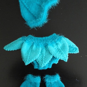 以下が含まれることがあります： ターコイズ色のニットのベビー服。帽子、セーター、ブーティ付き。セーターには葉の模様があります。