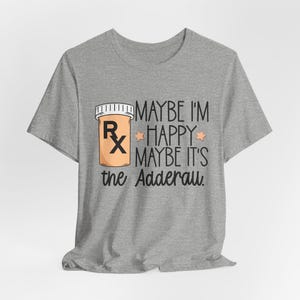 May include: A grey t-shirt with a prescription pill bottle graphic and the text "MAYBE I'M HAPPY MAYBE IT'S the Adderall." The pill bottle is tan with a white lid and the Rx symbol.