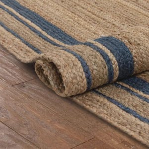 May include: A rolled-up jute rug with blue stripes. The rug is made of natural fibers and has a woven texture. The blue stripes run lengthwise across the rug.