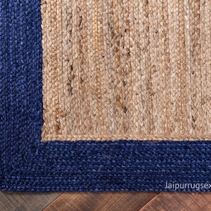 May include: A rectangular area rug featuring a natural tan braided jute center bordered by a thick, deep blue braided jute frame. The rug displays a textured, woven construction with visible fibers and the text jaipurrugsexporter in the corner.