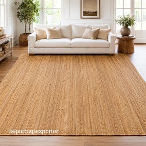 May include: A rectangular area rug made of natural tan jute fibers with a tightly woven, textured surface. The rug features a consistent, linear braided pattern throughout its entire length. The text "Jaipurrugsexporter" is visible in the bottom left corner.