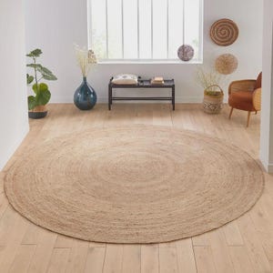 May include: A large, round jute rug in a neutral beige color. The rug has a spiral design and is placed on a light-colored wooden floor. The rug is a home decor item, suitable for living rooms or bedrooms.