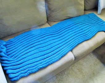 Könnte beinhalten: Eine blaue gestrickte Wolldecke mit Rippenstruktur liegt auf einem beigen Sofa.