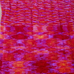 May include: A knitted blanket with a checkered pattern in shades of pink, red, and orange.