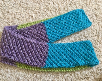 May include: A crocheted scarf with a purple, green, and blue color scheme. The scarf is made with a textured stitch.