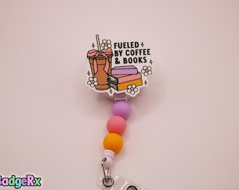 May include: A white badge reel with a colorful design. The design includes a coffee cup, books, and flowers, with the text "Fueled by Coffee & Books." The reel has a string of purple, pink, and yellow beads.