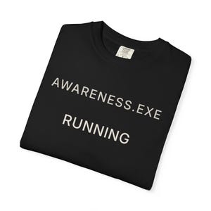 Puede incluir: Camiseta negra con las palabras "AWARENESS.EXE RUNNING" impresas en blanco. La camiseta está doblada y tiene una etiqueta en el cuello.
