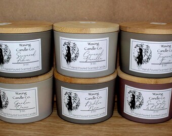 May include: Six scented candles with wooden lids. Each candle has a label with the text "Waxing Candle Co." and a unique scent name: Sugared Lemon, Caramel Vanilla, Tropical Fruit, Garden Oasis, Dahlia Noir, and Sea Salt & Orchid. Each candle is 3 oz.