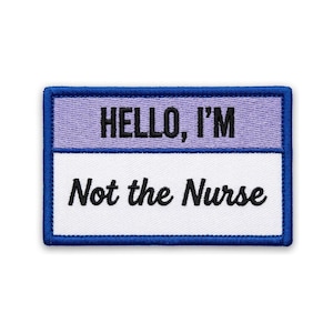 May include: Embroidered patch with the text "HELLO, I'M" above "Not the Nurse". The patch has a blue border, a lavender top section, and a white bottom section. Black text is used throughout.