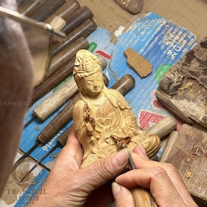 Female artisan meticulously sculpting a wooden Buddha figure in the workshop, highlighting the authentic handmade creation process and dedication to spiritual wood art by Tranquil Lotus Craft.