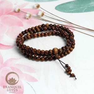 Aesthetic flat lay of wooden mala beads on white background with dried flowers. Zen altar decor idea and mindfulness tool display. Minimalist spiritual jewelry photography.