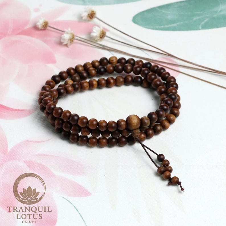 Aesthetic flat lay of wooden mala beads on white background with dried flowers. Zen altar decor idea and mindfulness tool display. Minimalist spiritual jewelry photography.