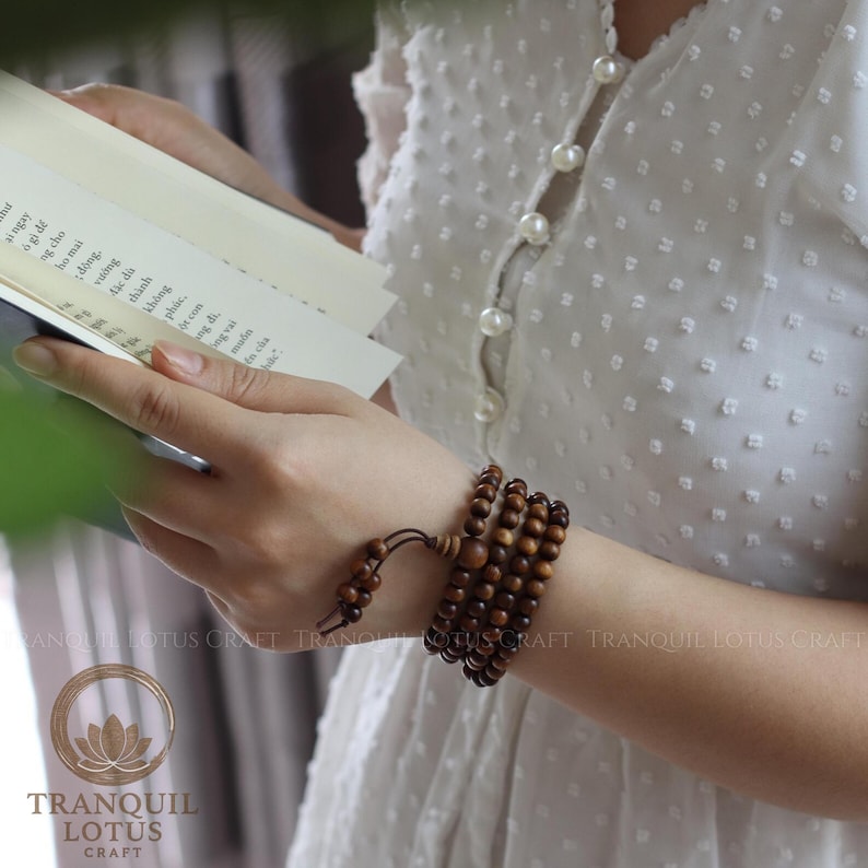 Woman reading a book wearing 108 bead mala wrapped as a multi-layer wood bracelet. Cozy mindfulness lifestyle and relaxation with scented Green Cypress jewelry. Boho spiritual gift for her.