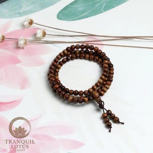 Aesthetic flat lay of wooden mala beads on white background with dried flowers. Zen altar decor idea and mindfulness tool display. Minimalist spiritual jewelry photography.