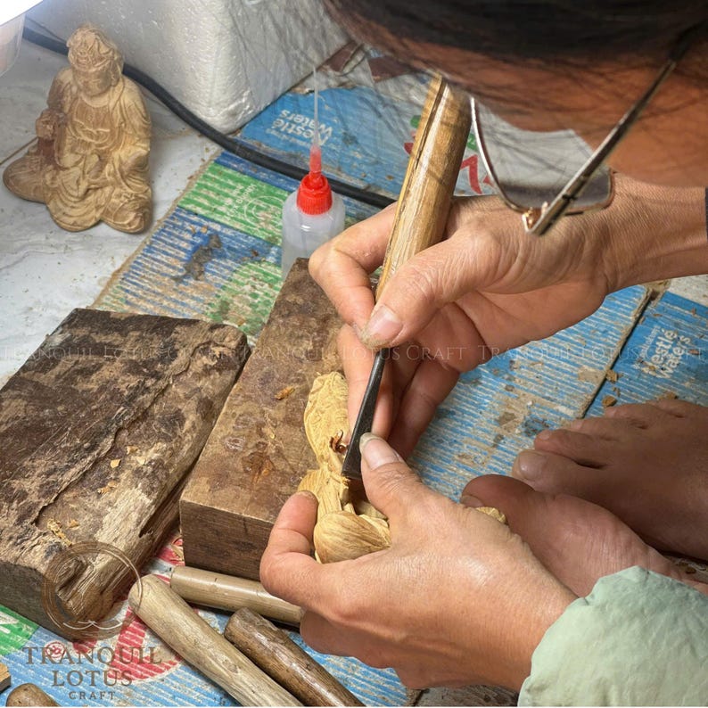 Female artisan meticulously sculpting a wooden Buddha figure in the workshop, highlighting the authentic handmade creation process and dedication to spiritual wood art by Tranquil Lotus Craft.